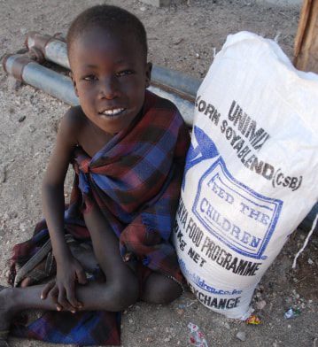 A child sitting outdoors next to a bag of food