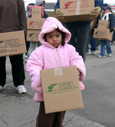 A small girl in a pink coat holding a box at an outdoor event