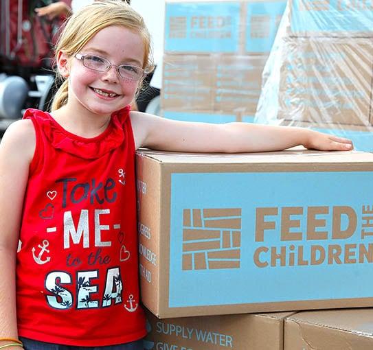 A child with her arm on a Feed the Children box outdoors