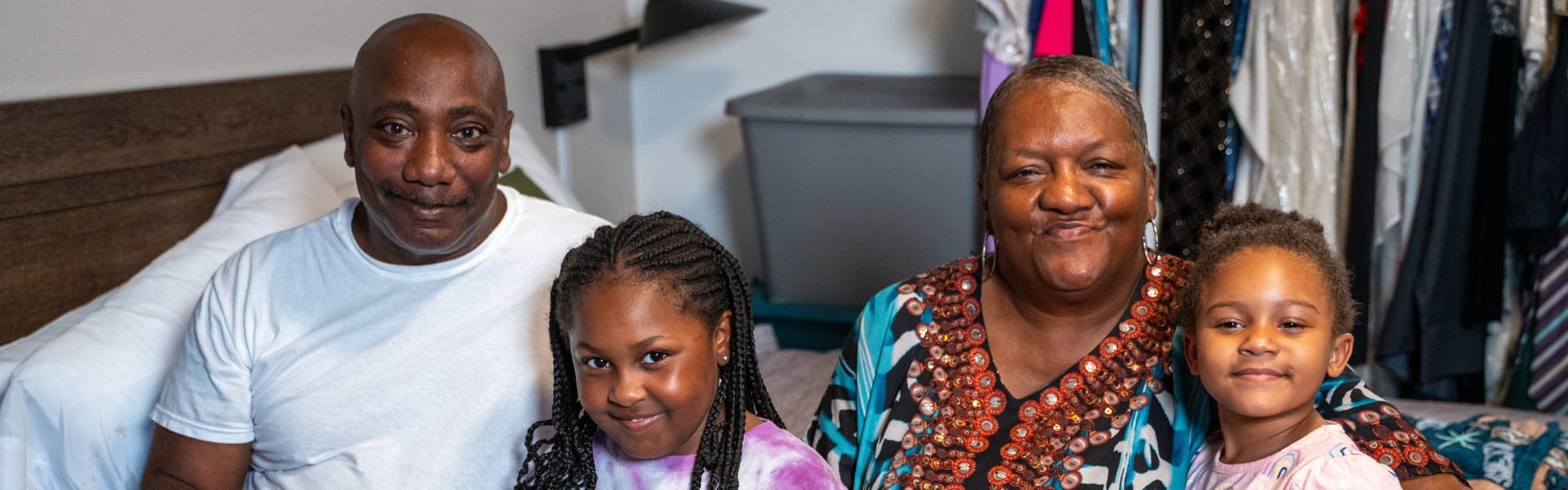 A family smiling while sitting on the bed