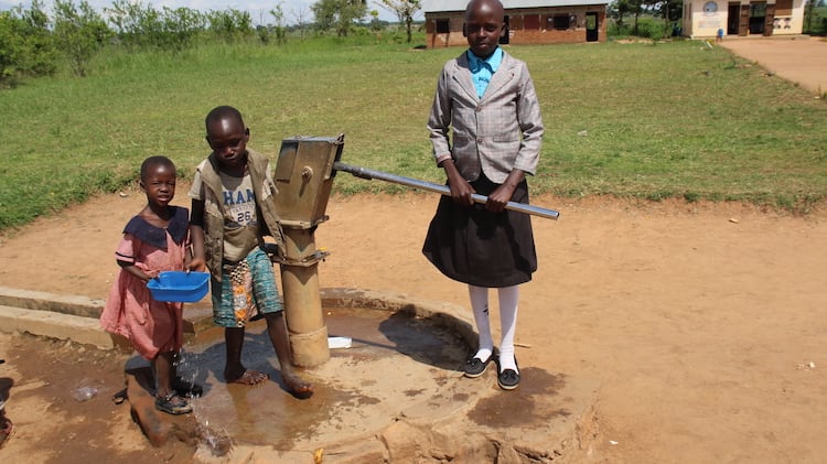 Three children pumping water outdoors
