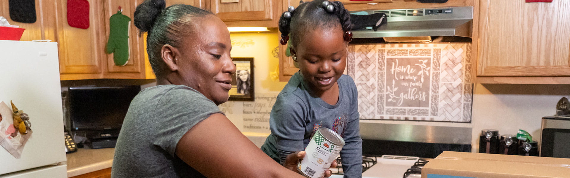 A mother and daughter holding food supplies in a kitchen