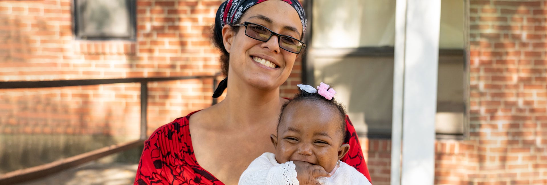 A woman and her baby smiling in front of a house