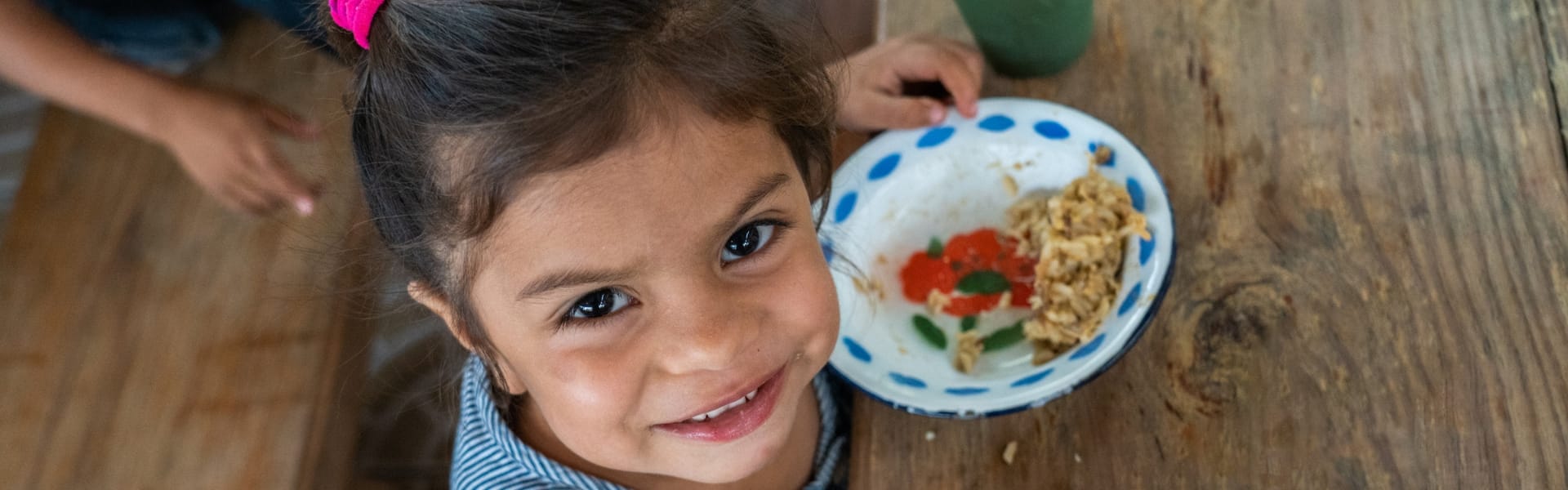 A child smiling with sitting at a table with a bowl of food