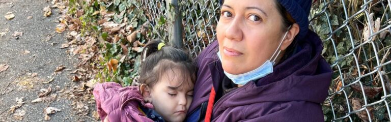 A mother and daughter sitting on the ground next to a fence outdoors