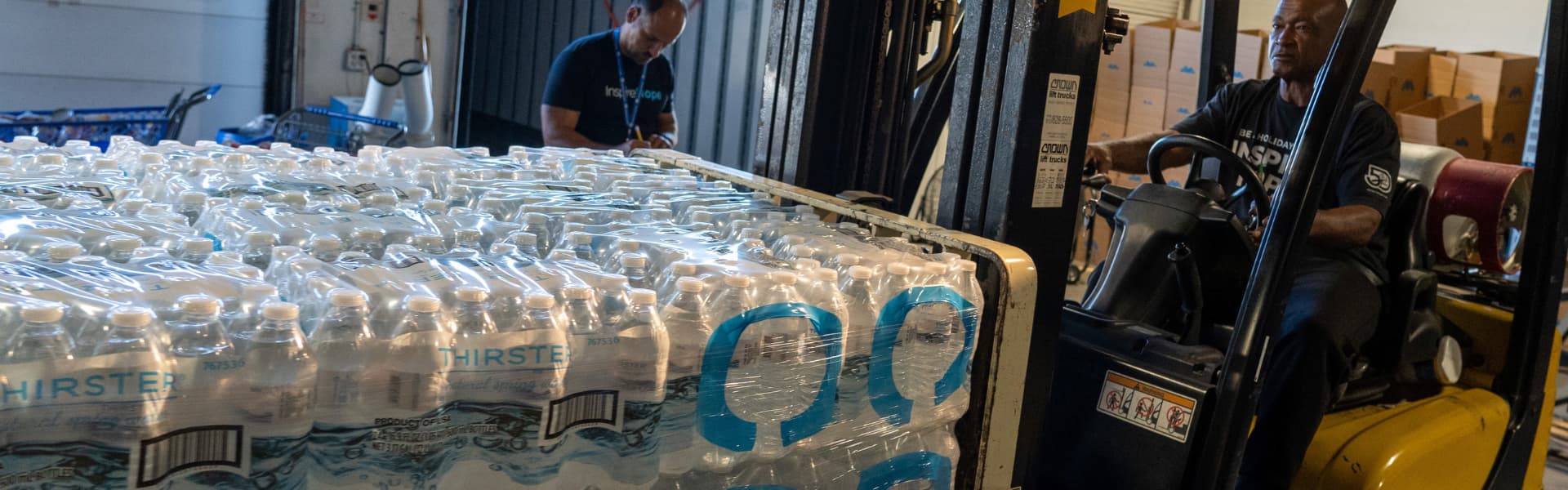 Workers moving water bottles with a forklift