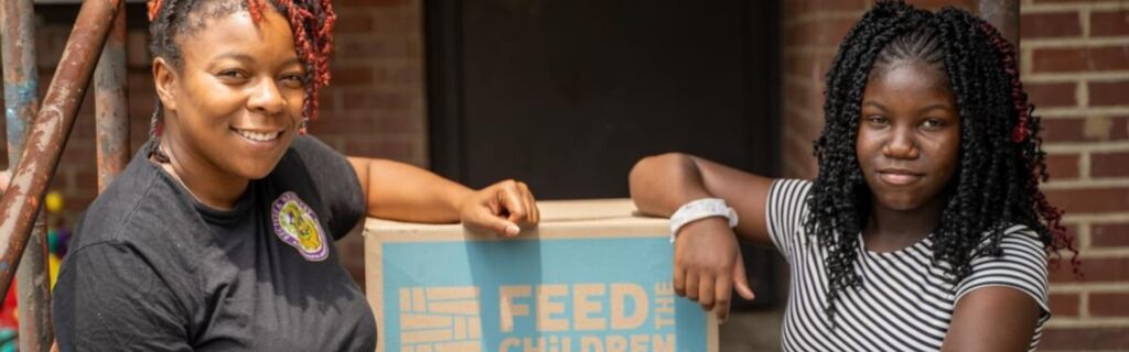 Two women with their arms resting on a feed the children box