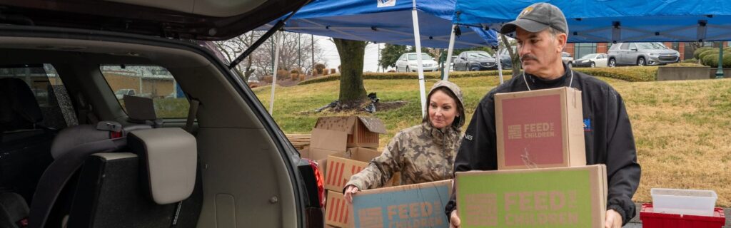 Two volunteers carrying boxes into the back of an suv