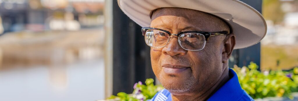 A man sitting outdoors wearing a hat and glasses