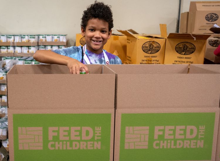 A child with boxes smiling outdoors at an event