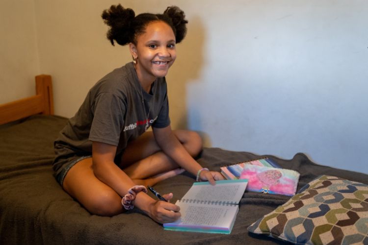 A child on a bed smiling while studying