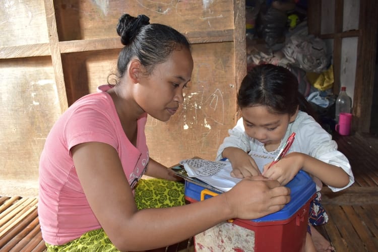 A woman and child writing on paper outdoors