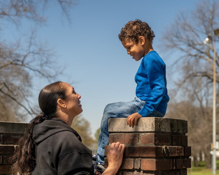 A child sitting on bricks looking at his mom