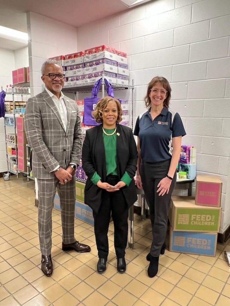 Three people posing in front of food supplies indoors