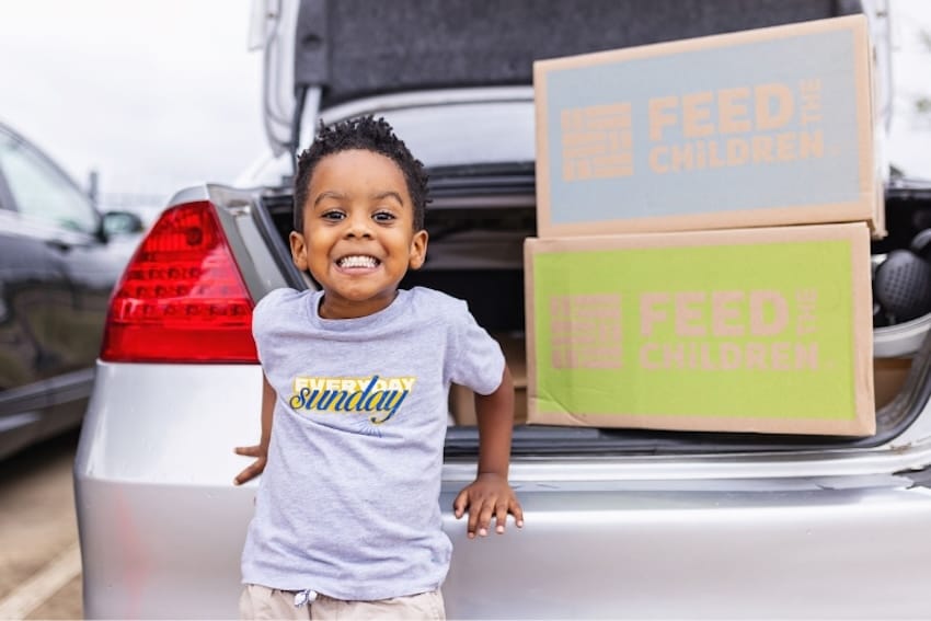 A boy smiling in front of a car with a box inside