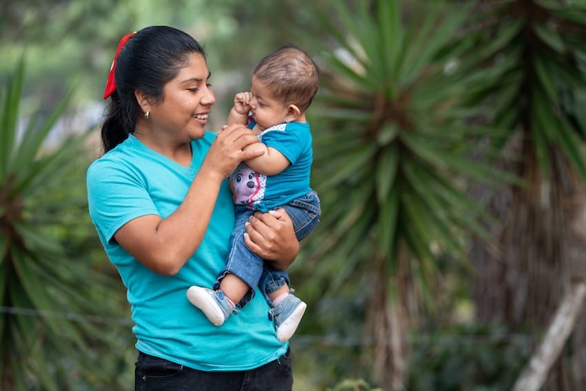 A mother holding her baby in front of trees