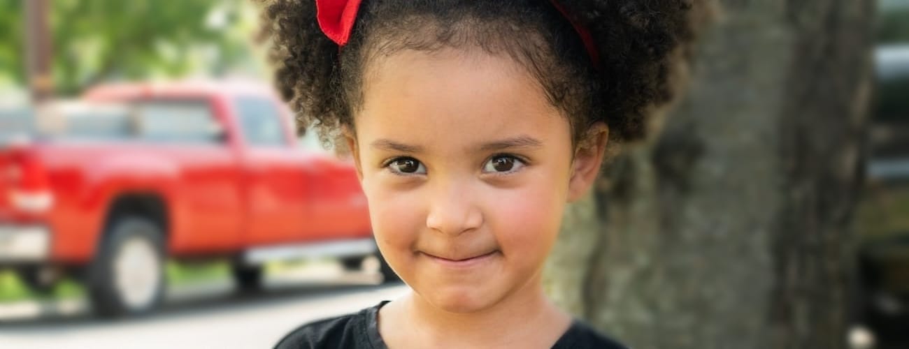 A child smiling while outdoors in front of a tree