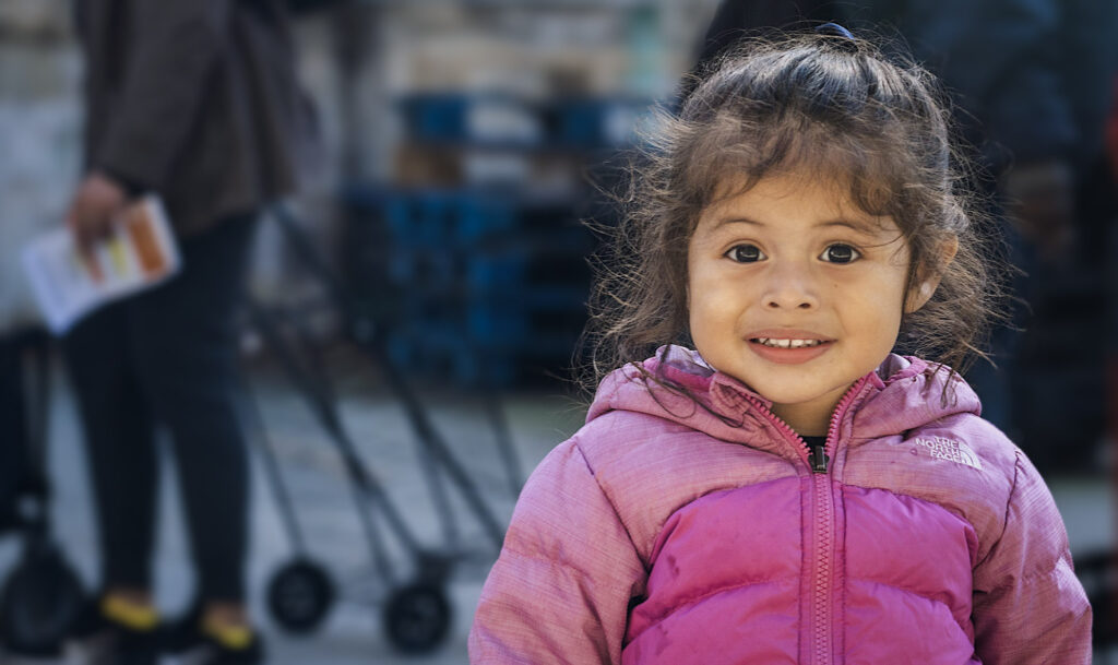 A child in a pink jacket at an outdoor event