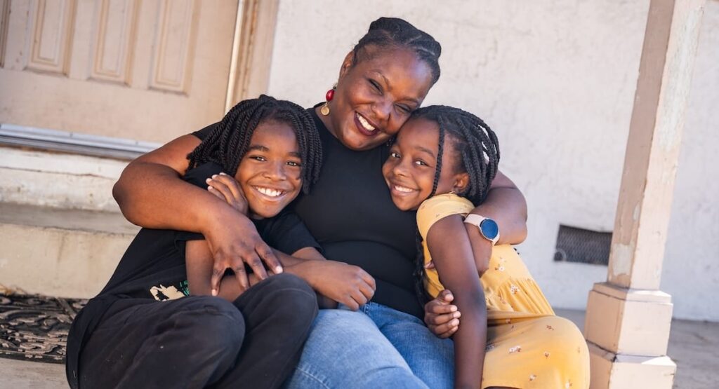 A mother and her two children hugging while sitting on the front porch of a house