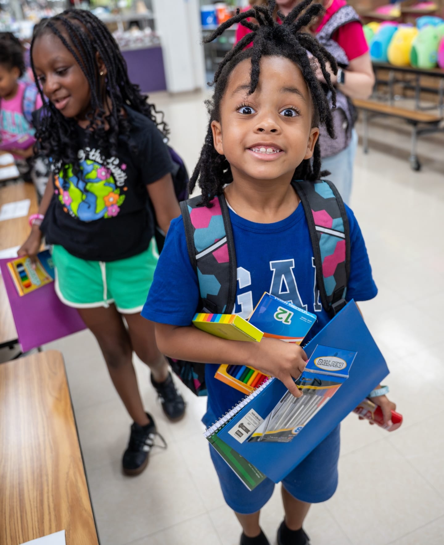 Two children standing with school supplies in a school.