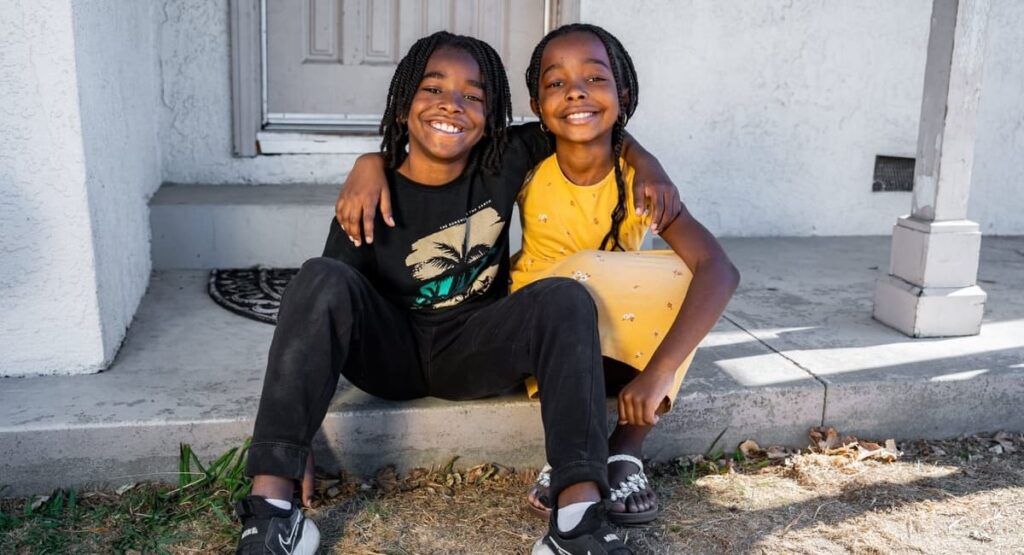 A brother and sister hugging while sitting on a porch