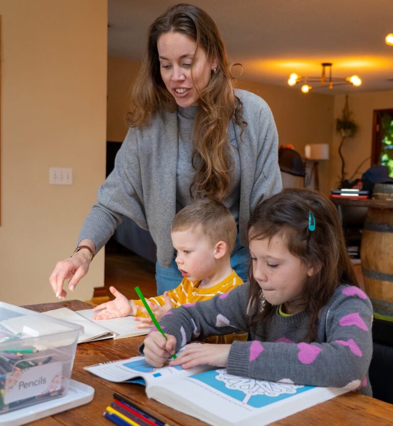 A woman with her two children at a table with school supplies.