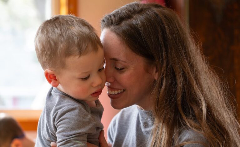 A woman holding her son while smiling indoors.