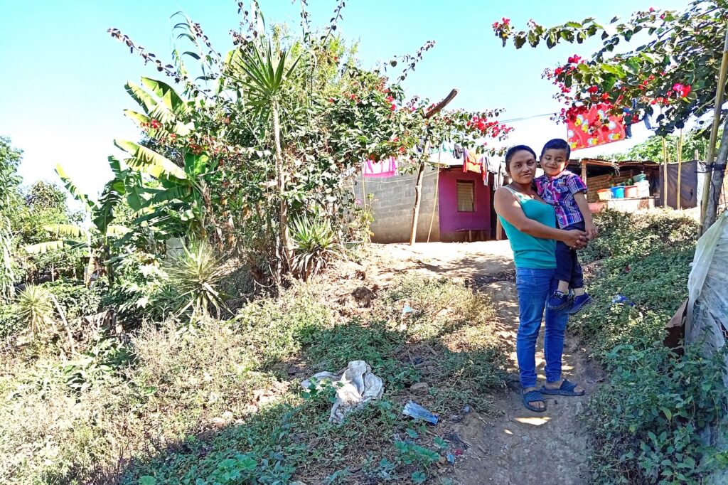 A mother and boy standing on a path near a home.