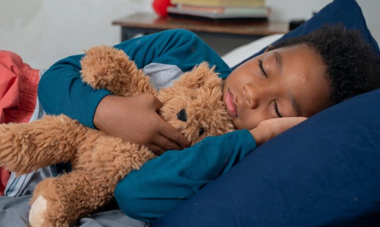 A child sleeping in bed with a teddy bear.