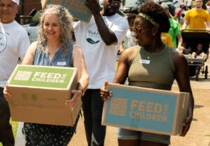 Two women carrying boxes at an outdoor event.