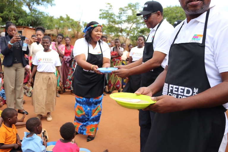 Adults handing out food bowls to children outdoors.