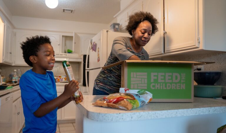 Rose and her son with a box of supplies in a kitchen.