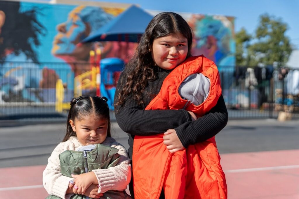 Two girls holding a vest and sleeping bag outdoors.