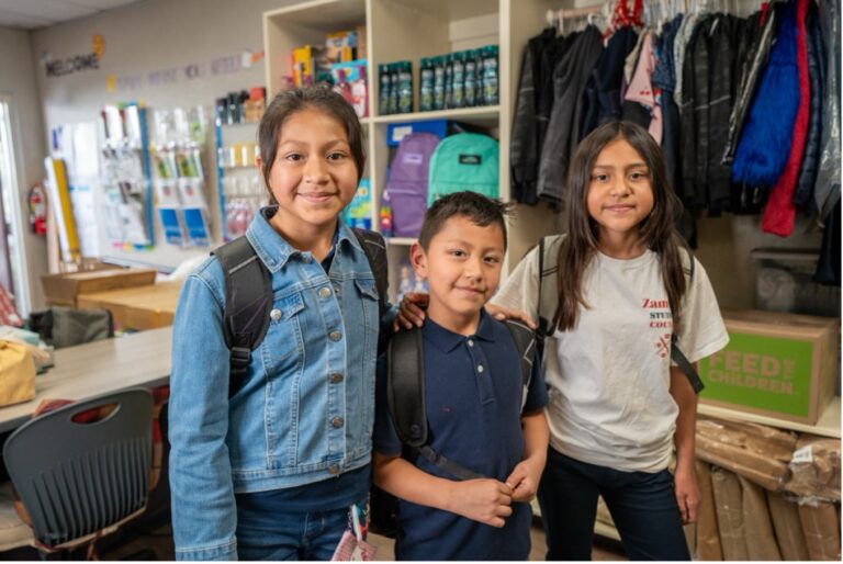 Three children standing in a school classroom.