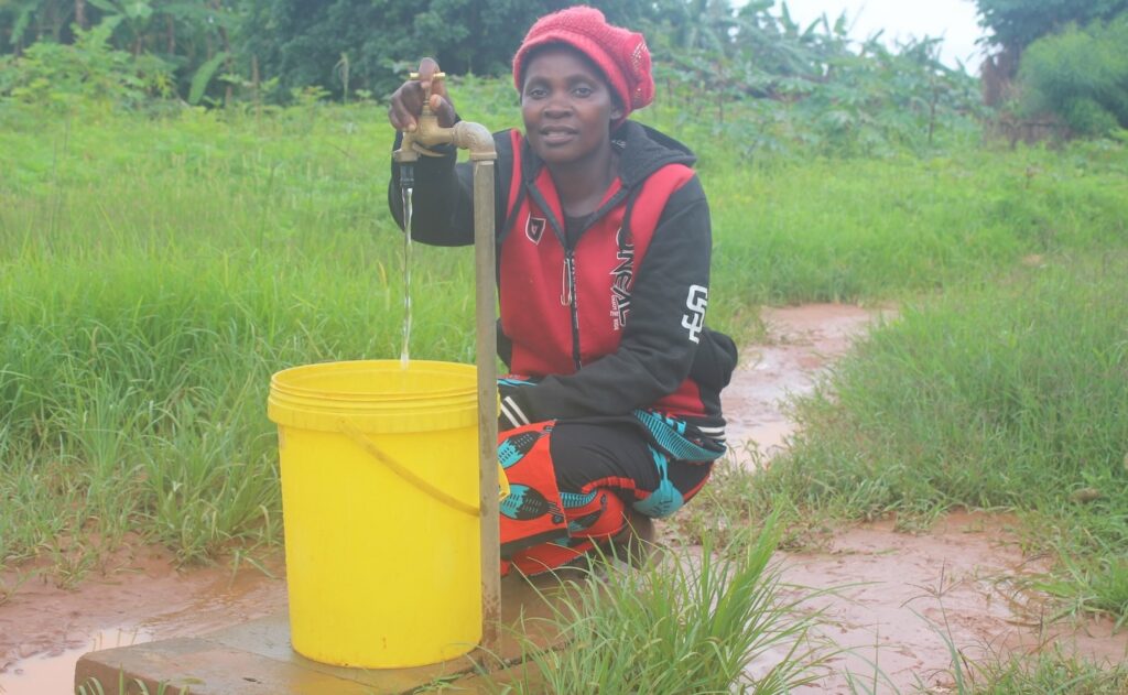 Catherine pouring water into a yellow bucket outdoors.