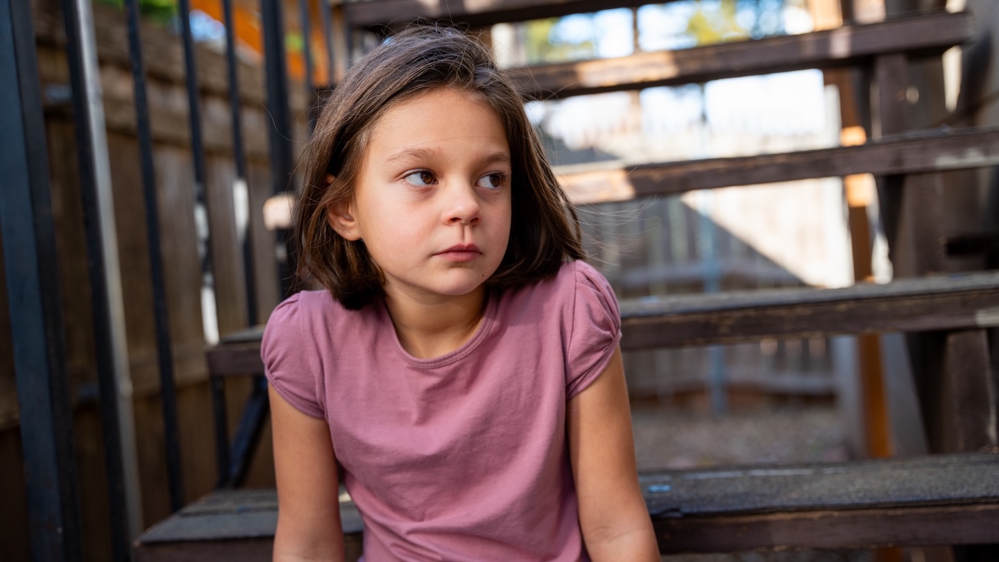 A young girl in a pink shirt sitting on stairs outdoors.