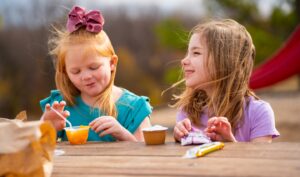 Two girls eating fruit cups at a table outdoors.