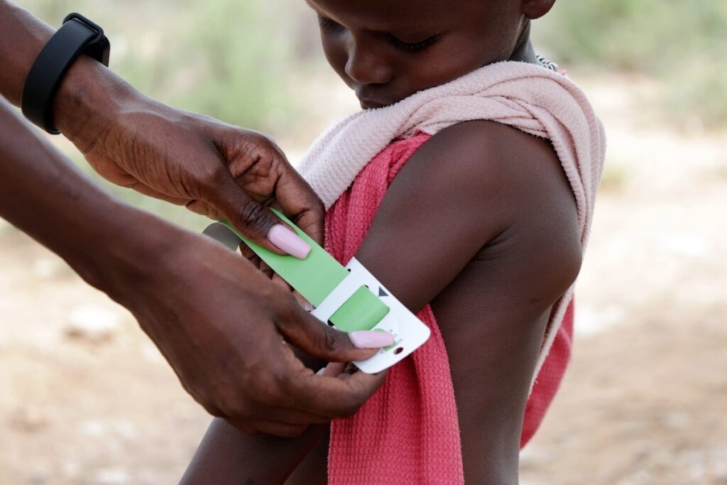 A child taking an arm circumference measurement in a group care session.