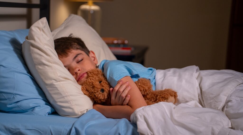 A young boy sleeping in bed with a teddy bear.