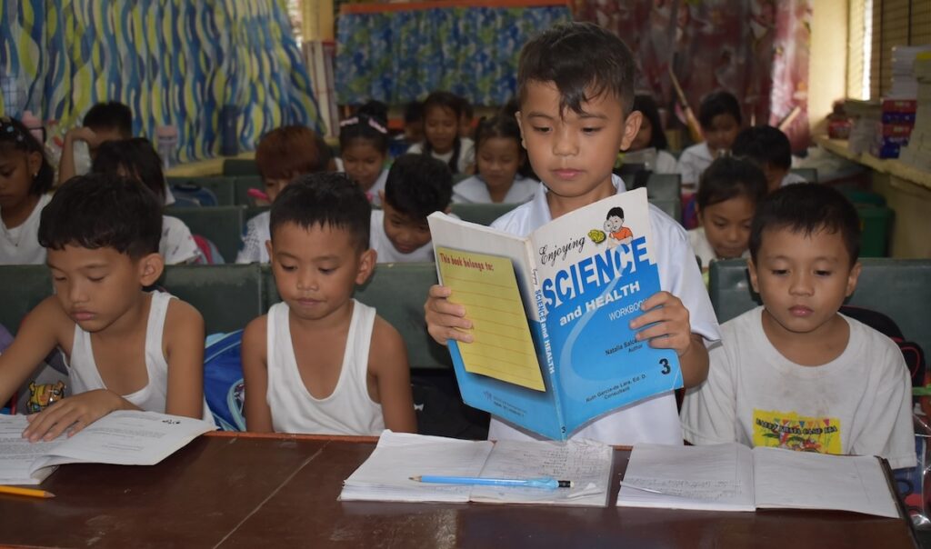 Jeecob reading a science book inside a classroom.