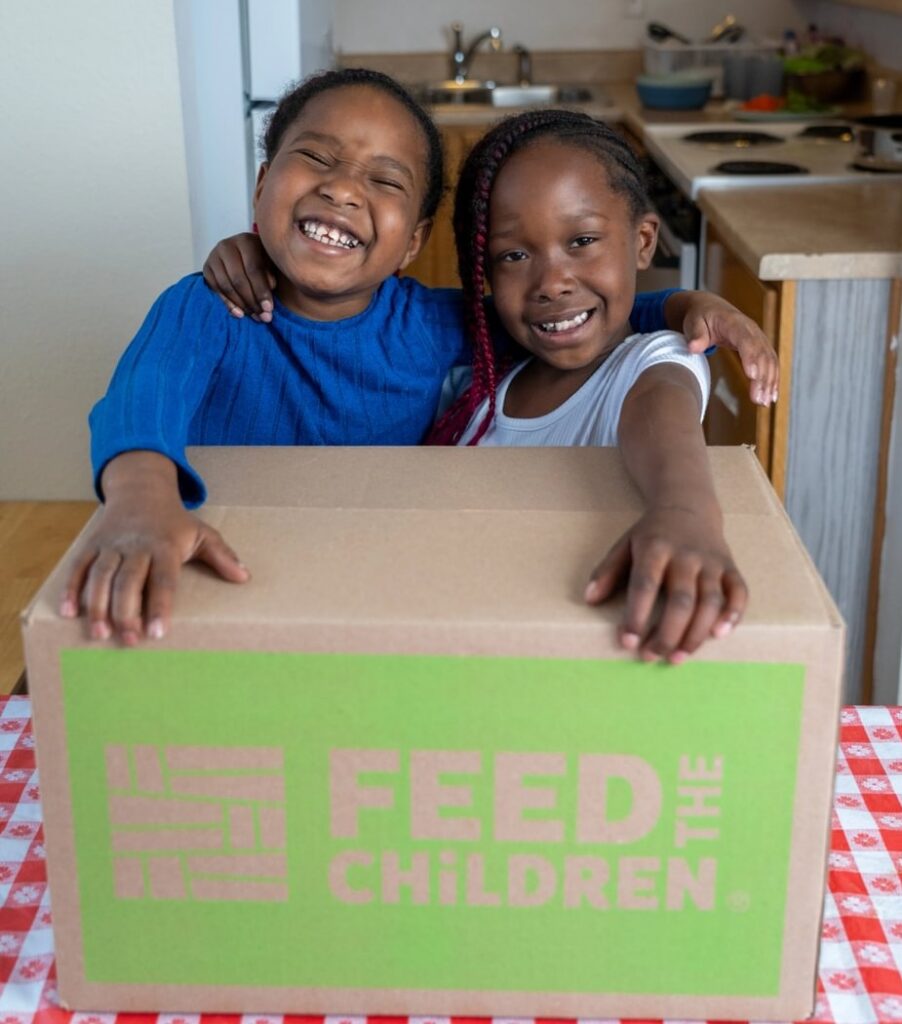 Two children holding a box sitting on a kitchen table.