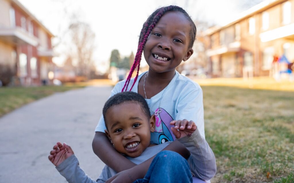 Two children holding each other on a sidewalk outdoors.