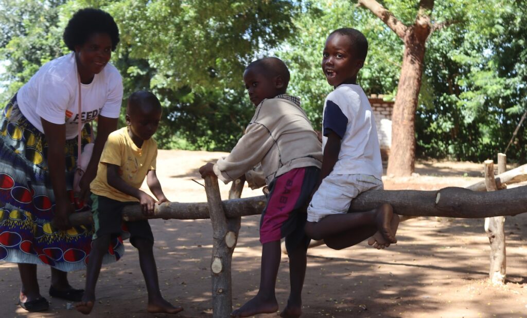 A group of children playing on a branch with a caretaker nearby.