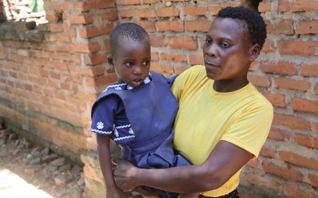 A woman in a yellow shirt holding a child in her arms outdoors.