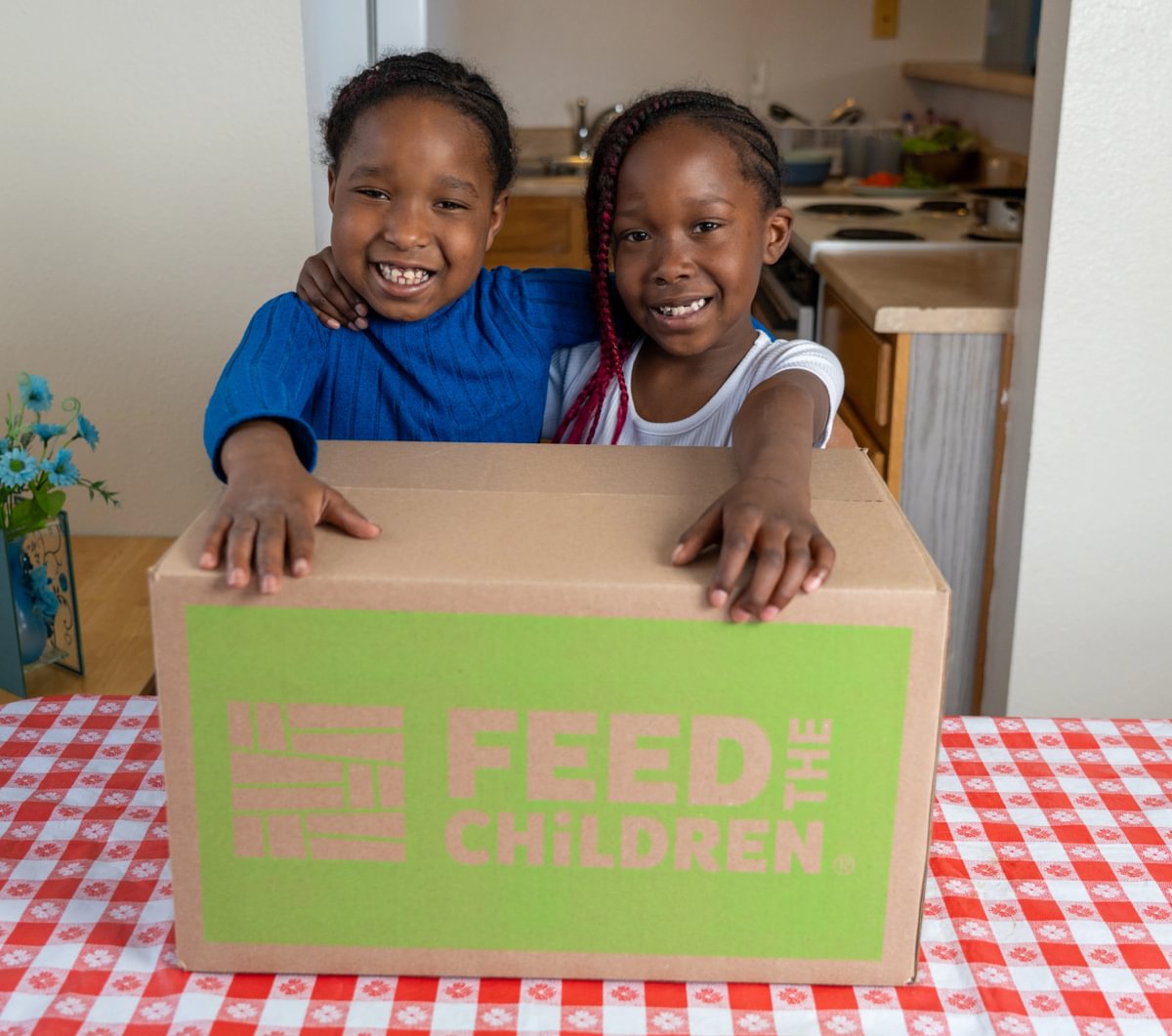 Two children holding a box of food on a table.