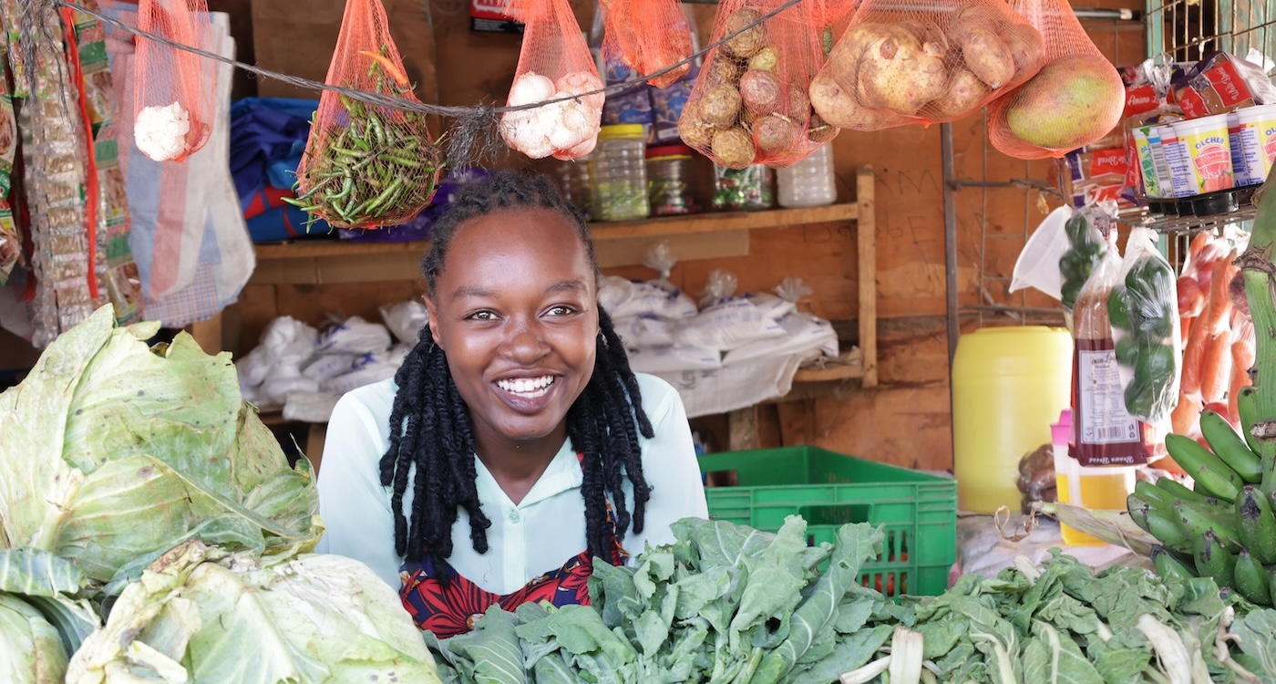 Joan smiling with vegetables around in her shop.