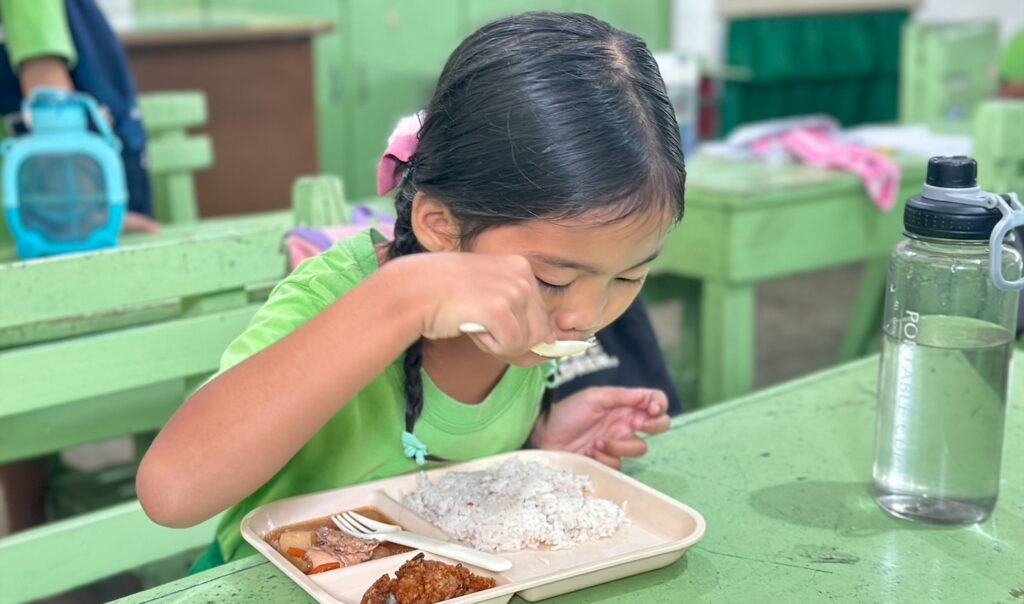 Khianna eating from a spoon at a table in a school.