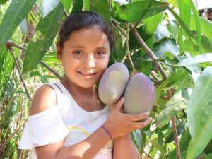 Daniela holding fruit attached to a tree branch.