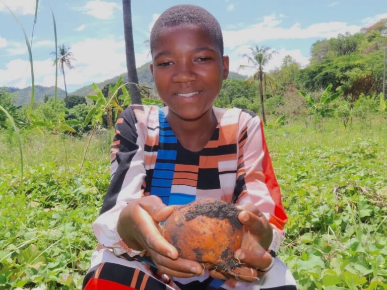 Halima holding food while standing in a field.