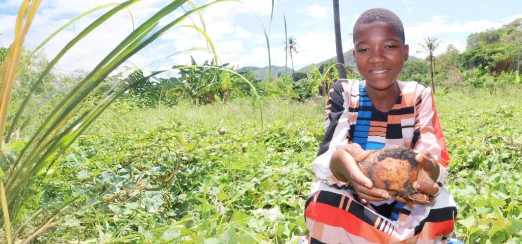 A child holding food on a sunny day in a field in Africa.